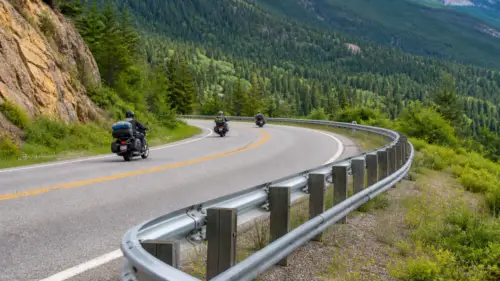 Motorcycles traveling on a mountain road beside a guardrail with a lower auxiliary rail