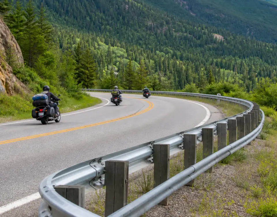 Motorcycles traveling on a mountain road beside a guardrail with a lower auxiliary rail