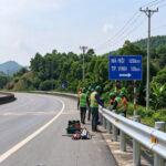 Road maintenance crew installing galvanized W-beam guardrail on a Vietnamese expressway, with Ninh Binh and Vinh destination signage
