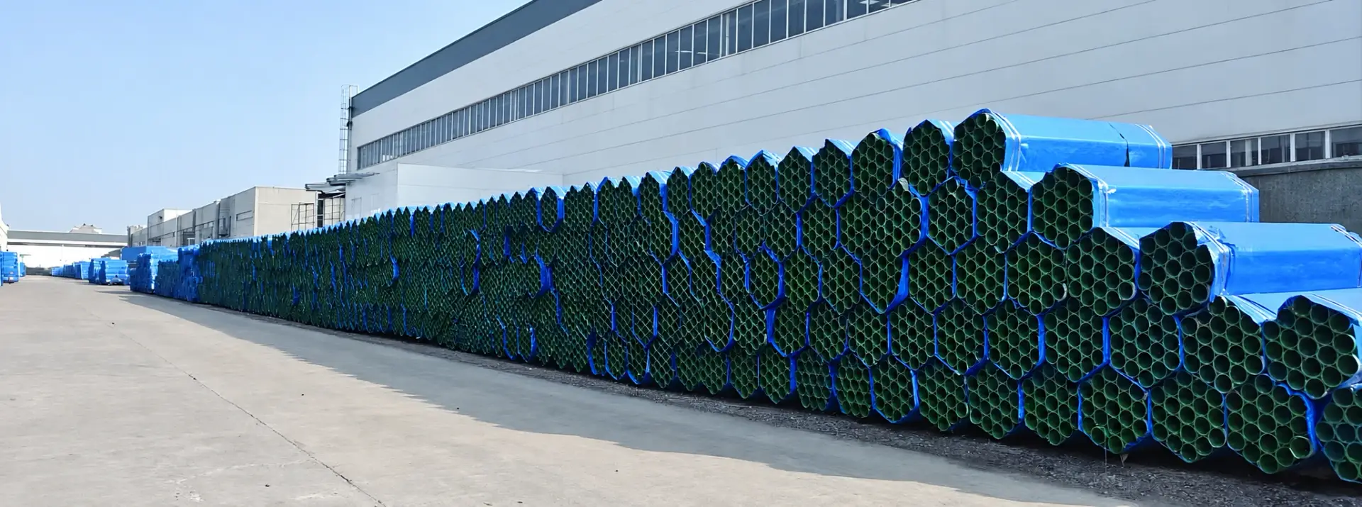 Bundled steel guardrail posts stored outdoors beside the factory workshop