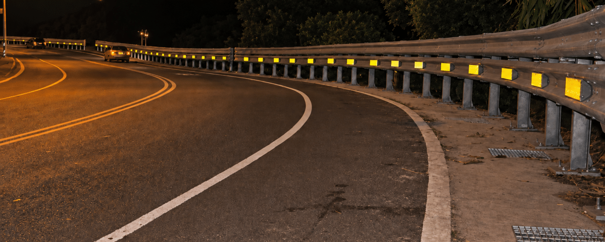Nighttime highway curve with a guardrail and retroreflective delineators